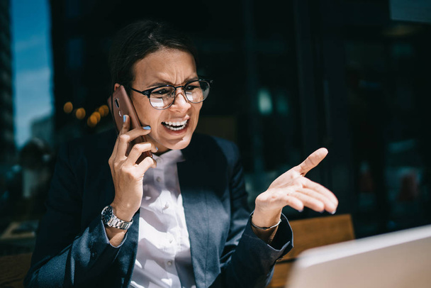 Angry woman in optical eyewear for vision correction received email with accounting report of company via application on laptop and calling to corporate director for shouting and pour out of rage - Foto, Bild