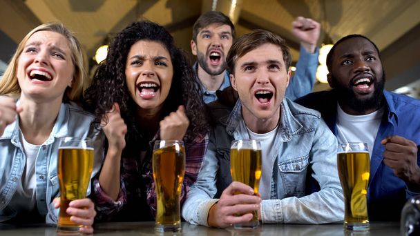 Joyful team supporters screaming watching tv in beer pub, celebrating goal - Фото, изображение