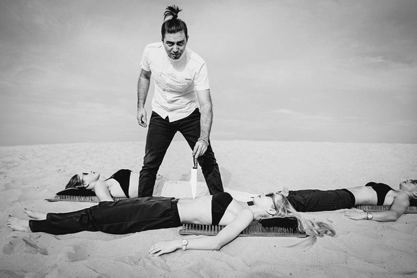 極端なトレーニング - 男(グル、マスター)は、砂漠で屋外で女性の胃にナイフを保ちます。極端な趣味、意志の力、トレーニング、ヨガの概念 - 写真・画像