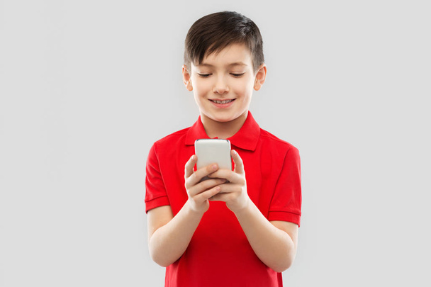 smiling little boy in red t-shirt using smartphone - Фото, изображение