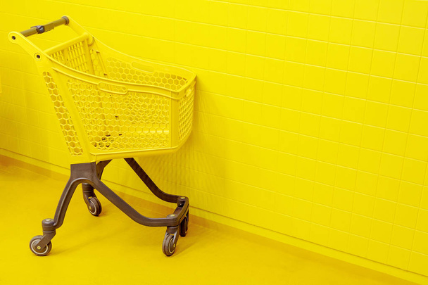 Koncept nakupování. Prázdný žlutý vozík s potravinami stojí ve žlutém patře na pozadí žluté zdi - Fotografie, Obrázek