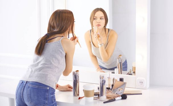 Hämmästyttävä nuori nainen tekee hänen meikki edessä peili. Muotokuva kaunis tyttö lähellä kosmeettinen pöytä - Valokuva, kuva