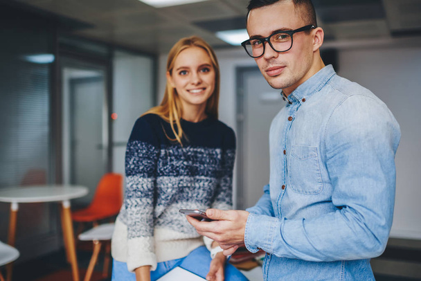 Portrait of professional colleagues dressed in casual wear looking at camera while working together in office interior.Two hipster students standing in coworking space.Young man with cellular in hand - Foto, Bild