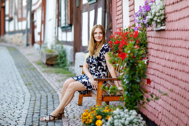 Mooie jonge vrouw met lange haren in zomerjurk die een wandeling gaat maken in de Duitse stad. Happy girl genieten wandelen in schattige kleine fachwerk stad met oude huizen in Duitsland. - Foto, afbeelding