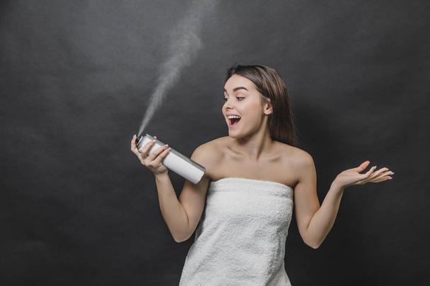 Attractive woman spraying hairspray isolated on black background. Head and shoulders, studio, indoors. - Фото, изображение