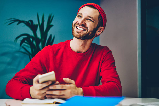 Χαρούμενος καυκάσιος χιλιετής άνδρας χαρούμενος για την εγκατάσταση δωρεάν εφαρμογής στο κινητό τηλέφωνο, επιτυχημένος hipster blogger τύπος ικανοποιημένος με το smartphone και σύνδεση στο internet σε συνεργασία spac - Φωτογραφία, εικόνα