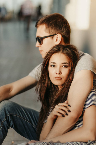Happy young couple in love teenagers friends dressed in casual style sitting together on city street. Beautiful asian girl, multiracial people - Foto, Imagem