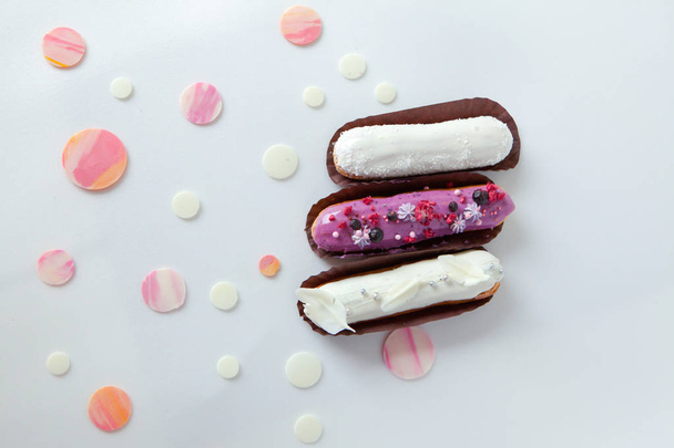 A set of three eclairs with different fillings and design isolate on a white surface decorated with drops of white chocolate - Фото, зображення
