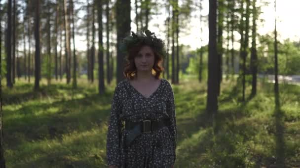 spazieren gehen: rothaarige junge Frau im Kranz während des traditionellen lettischen ligo Mittsommertages - kaukasisches weißes Mädchen in einem gepunkteten Sommerkleid mit Gürtel im sonnigen Sonnenuntergang - Filmmaterial, Video