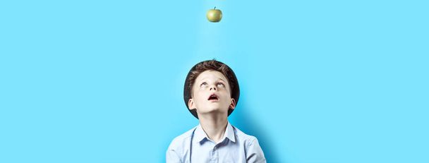 Surprised boy in a light shirt looks up. There on him falls green Apple, as a symbol of great ideas - Valokuva, kuva