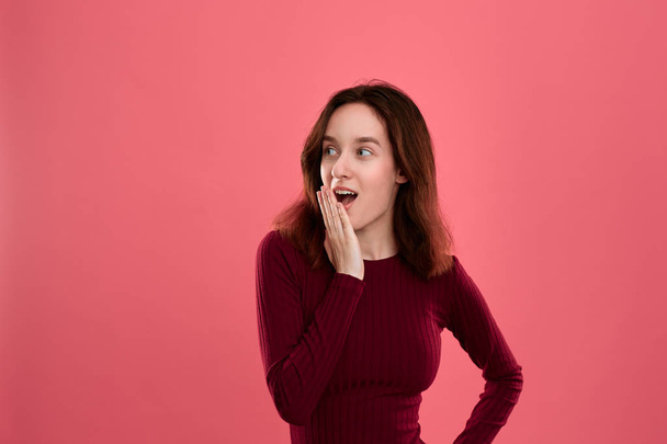 Surprised young lady standing isolated over dark pink background with hands raised close to mouth expressing emotion of shock. - Photo, Image