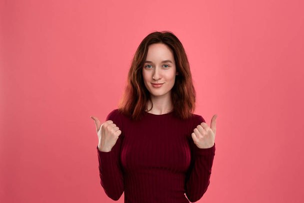 Happy young lady standing isolated over dark pink background with thumbs up giving positive appraisal. - Photo, Image