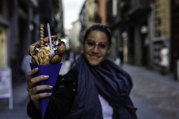 Beautiful woman holding a bubble waffle with ice cream and candi - Photo, Image