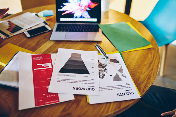 Pulpit z papierami i dokumentacją do pracy z księgowością, nowoczesny laptop stojący na stole w pobliżu notatników infograficznych i papeterii do nauki lub tworzenia biznes planu - Zdjęcie, obraz
