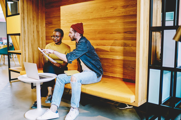 Skilled male and female hipsters reading information from paper cooperate on homework project, multiracial colleagues discussing business plan talking and discussing ideas together in offic - 写真・画像