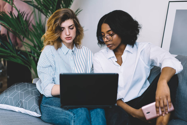 African american young woman with caucasian colleague cooperating on development own design website at laptop device using wireless internet working remotely at home in modern apartment - 写真・画像