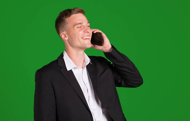 Young man in a suit talking on a smartphone, isolated on a green background. - Photo, image