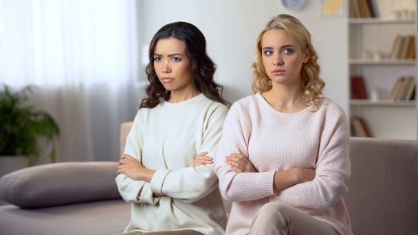 Two offended women sitting on sofa with hands crossed, conflict between friends - 写真・画像