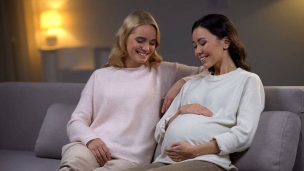 Smiling pregnant woman holding tummy, sitting with friend, baby expectation - Fotoğraf, Görsel