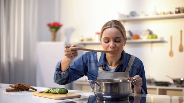 Beautiful lady tasting soup while cooking, preparing food for dinner, dieting - Fotografie, Obrázek