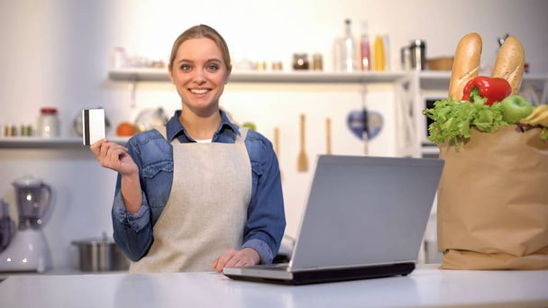 Usměvavá žena držící kreditní kartu v kuchyni, nákup a dodávky potravin online - Fotografie, Obrázek