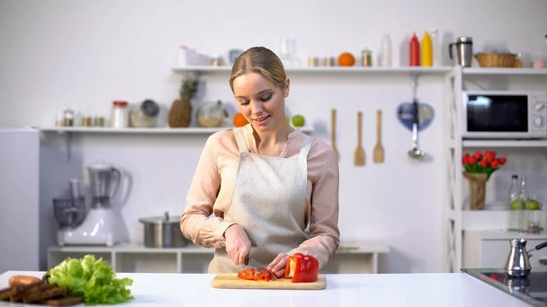 Pretty female slicing red bell pepper, cooking salad for dinner, raw food diet - Fotoğraf, Görsel