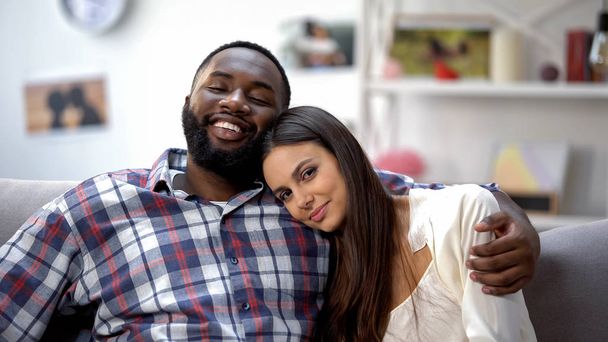 Smiling multiethnic couple hugging on sofa, relaxing together, tender feelings - Foto, immagini