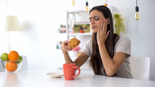 Woman having lunch, eating croissant with coffee, feeling toothache from sweets - Foto, immagini