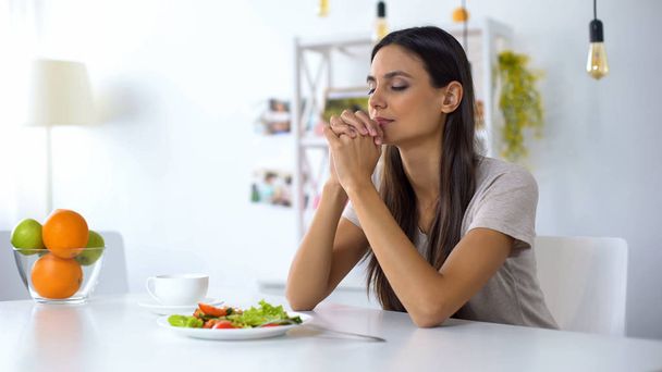Nice lady praying, blessing God for dinner, eating healthy vegetarian salad - Valokuva, kuva