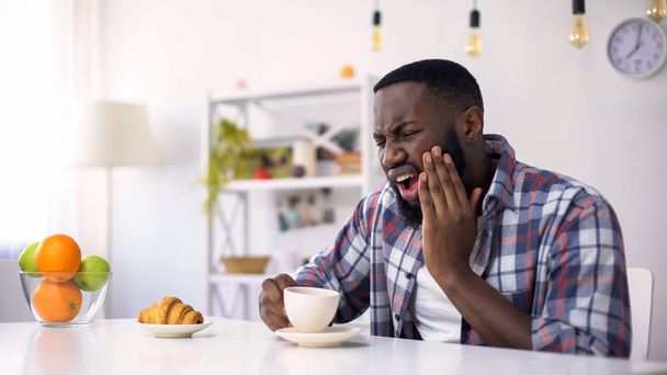 Afro-American man having dental ache, reaction on hot coffee, sensitive teeth - Φωτογραφία, εικόνα