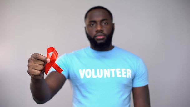 African-American volunteer showing red ribbon to camera, HIV/AIDS symbol - Foto, Imagen