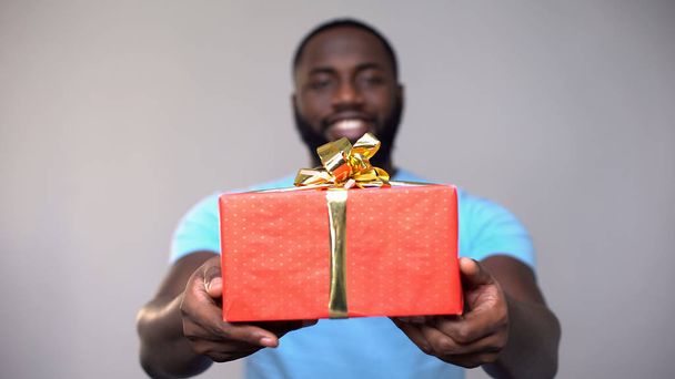 Black male volunteer showing charity gift box at camera, present for poor kids - Fotó, kép