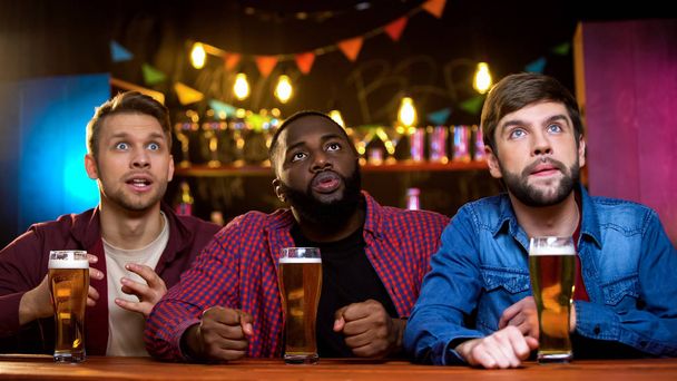 Τρεις άνδρες φίλοι βλέποντας έκτακτη είδηση σε μεγάλη οθόνη στο μπαρ, βραδινή αναψυχή - Φωτογραφία, εικόνα
