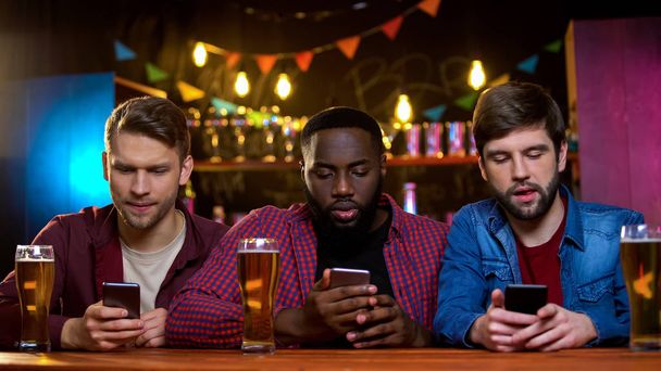 Multiethnic friends using smartphones sitting in pub, problem with communication - Foto, imagen