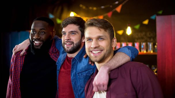 Cheerful multiethnic guys hugging, spending time in bar, leisure activity - Foto, imagen
