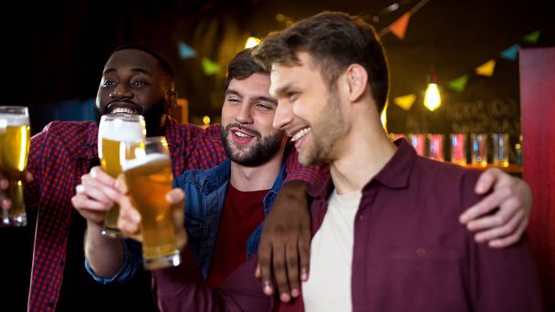 Drunk multiethnic friends clinking beer glasses, spending time in pub, party - Zdjęcie, obraz