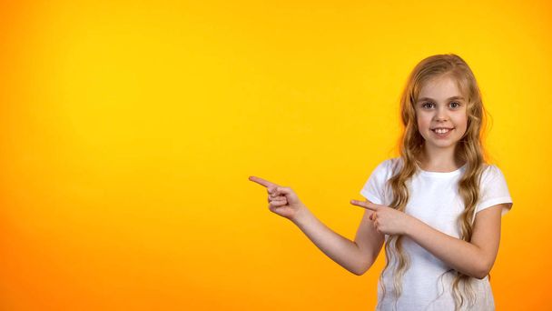 Smiling girl pointing at orange background, advertisement template, promotion - Foto, afbeelding