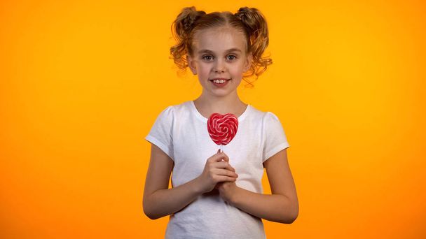 Adorable schoolgirl holding heart-shaped lollipop, happy child, confectionery - Foto, immagini