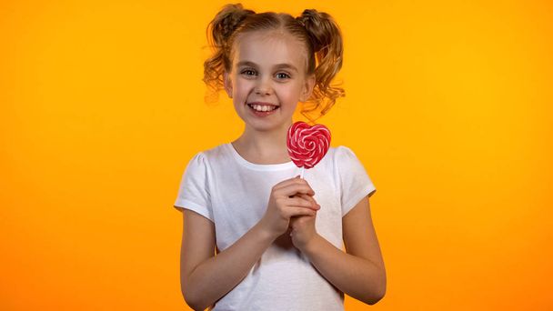 Pretty candy girl holding heart-shaped lollipop and smiling to camera, happiness - Фото, зображення