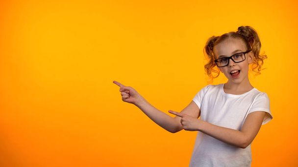 Pretty nerd girl in glasses pointing at orange background, education opportunity - Фото, изображение
