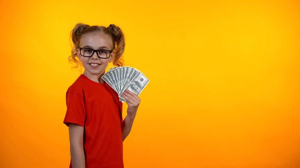 Pretty teenage girl in spectacles showing bunch of dollar bills, earning money - Foto, afbeelding