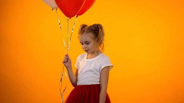 Beautiful little girl holding balloons and thinking, preteen kid feeling shy - Foto, imagen