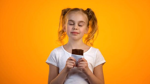 Cute schoolgirl enjoying taste of delicious chocolate, happy childhood, emotions - Fotó, kép