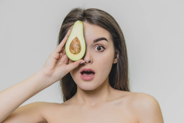 Close-up portrait beautiful girl with half avocado. She looks astonished. - Valokuva, kuva