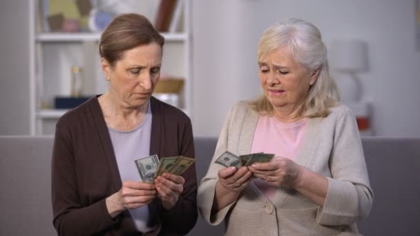Senior female holding dollars complaining friend on poverty problem, low income - Filmati, video