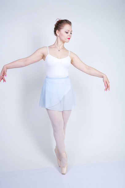мила біла дівчина в балетному одязі вчиться бути балериною на білому тлі в студії. плюс розмір молода жінка мріє стати танцівницею
. - Фото, зображення