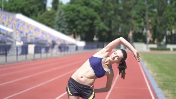 4K. νεαρή αθλητική γυναίκα που τεντώνει το σώμα πριν τρέξει στο στάδιο. Κλίσεις - Πλάνα, βίντεο