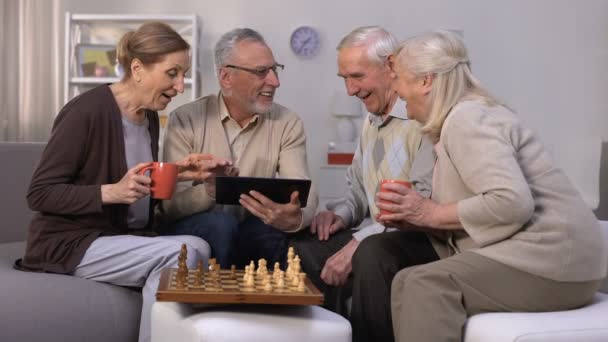 Elderly man showing friends new project on tablet pc, chess play brake, company - Footage, Video