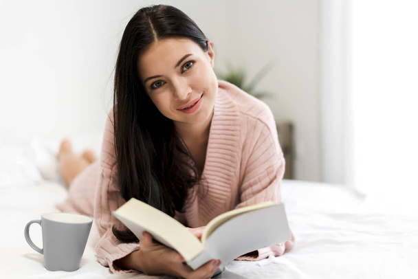 junge Frau entspannt sich und liest Buch zu Hause im Bett - Foto, Bild