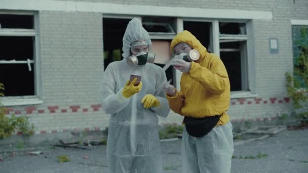Two scientists put on a respirator and conduct research. The environment is in danger. Coronavirus in a pandemic, COVID-19. Two girls in protective suits from radiation. Enter the data into the phone. - Materiał filmowy, wideo